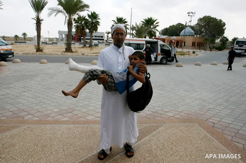 A Palestinian man carries his child, who medics said was wounded during the Israeli offensive on Gaza Strip, waits to be given the permission to cross into Egypt at the Rafah border crossing in the southern Gaza Strip, o...