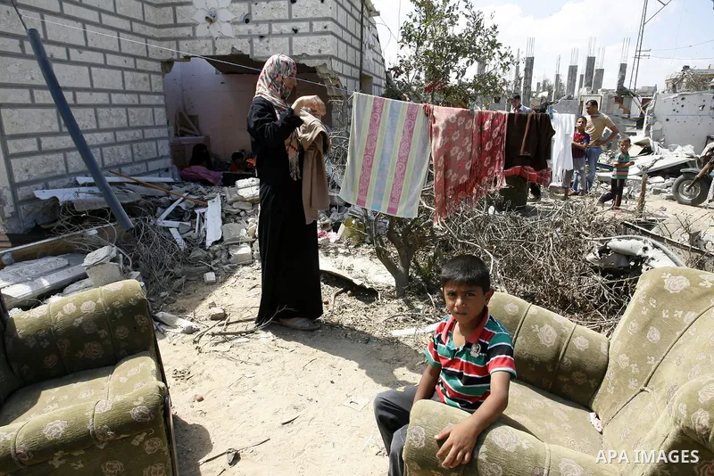 A Palestinian woman works as her son plays at their destroyed house in Khan Yunis in the southern Gaza Strip on September 11, 2014. Israel's deputy foreign minister,Tzahi Hanegbi , warned that Hamas was likely to resume...