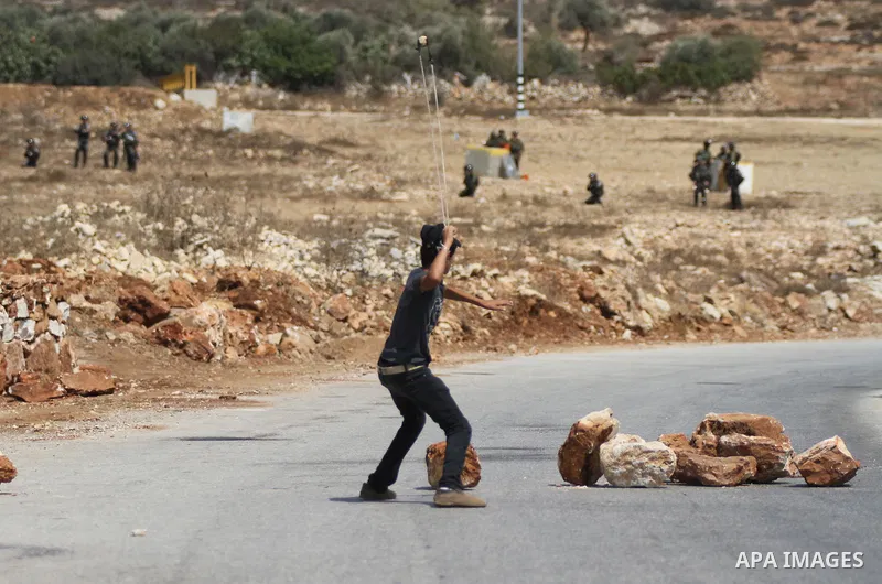 A Palestinian protester uses a sling shot to hurl a stone at Israeli troops during clashes at a weekly protest against Jewish settlements, in the West Bank village of Nabi Saleh, near Ramallah, September 12, 2014. Photo...