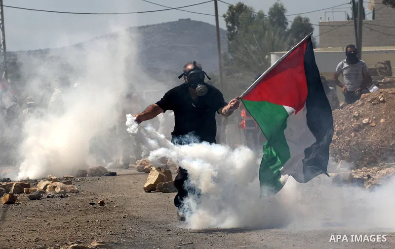 A Palestinian protester waves a national flag as he throws back a tear gas canister during clashes with Israeli security forces following a protest in the village of Kfar Qaddum, near the northern city of Nablus, in the...