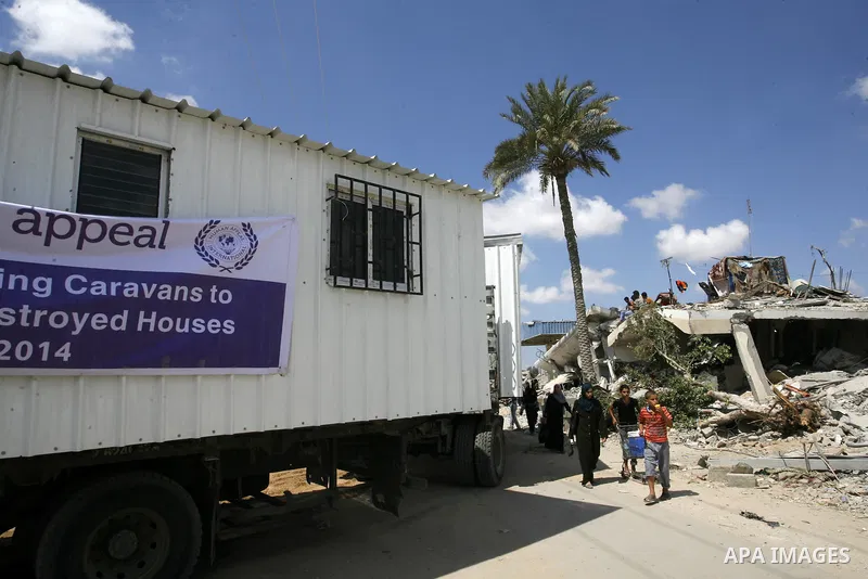 Palestinian walk past containers donated by Human Appeal for Palestinians, as temporary replacements for the houses that were destroyed during a seven-week Israeli offensive, in the east of Khan Younis in the southern Ga...