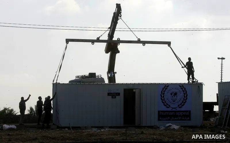 Workers place containers donated by Human Appeal for Palestinians, as temporary replacements for the houses that were destroyed during a seven-week Israeli offensive, in the east of Khan Younis in the southern Gaza Strip...