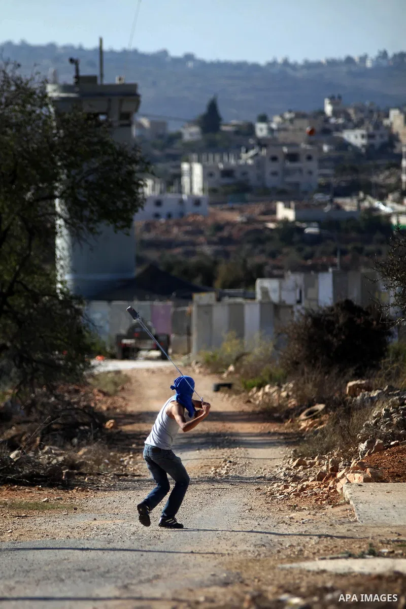 A Palestinian protester uses a slingshot to hurl a stone towards Israeli security forces during clashes at a protest against the Jewish settlement of Ofra, in the West Bank village of Silwad, near Ramallah September 26,...