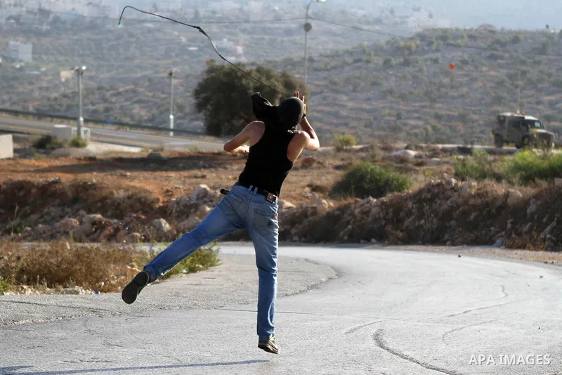 A Palestinian protester uses a slingshot to hurl a stone towards Israeli security forces during clashes at a protest against the Jewish settlement of Ofra, in the West Bank village of Silwad, near Ramallah September 26,...