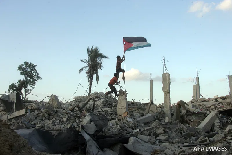 Palestinian children hold their national flag on the rubble of houses which destroyed during a seven-week Israeli offensive, in the east of Khan Younis in the southern Gaza Strip October 1, 2014. An open-ended ceasefire...