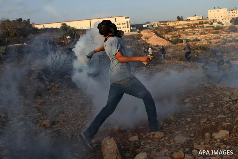 A Palestinian protester throws back a tear gas canister towards Israeli security forces during clashes at a protest to show solidarity with al-Aqsa mosque, outside Israel's Ofer military prison near the West Bank city of...