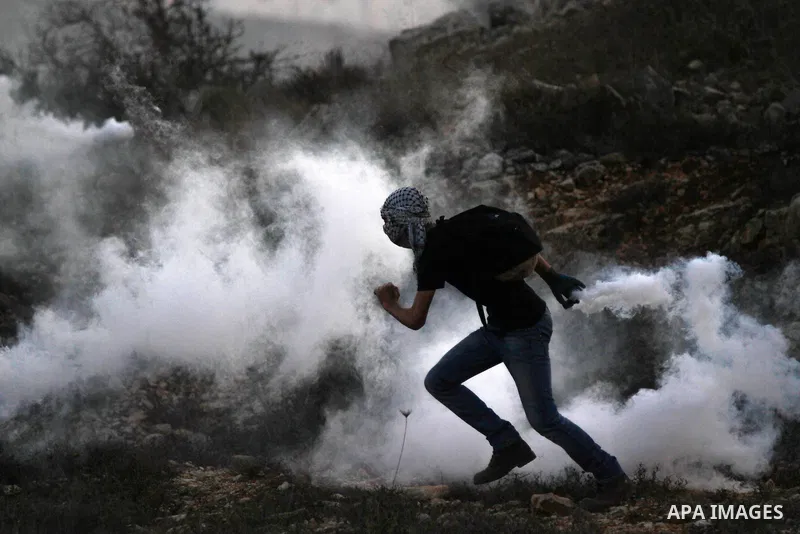 A Palestinian protester runs for cover from tear gas fired by Israeli security forces during clashes at a protest to show solidarity with al-Aqsa mosque, outside Israel's Ofer military prison near the West Bank city of R...