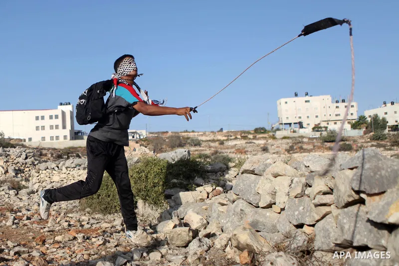 A Palestinian protester uses a sling shot to hurl stones towards Israeli security forces during clashes at a protest to show solidarity with al-Aqsa mosque, outside Israel's Ofer military prison near the West Bank city o...
