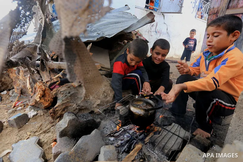 Palestinian children warm themselves by a fire inside their house that witnesses said was destroyed during a seven-week Israeli offensive, on a rainy day in the east of Gaza City October 19, 2014. An open-ended ceasefire...