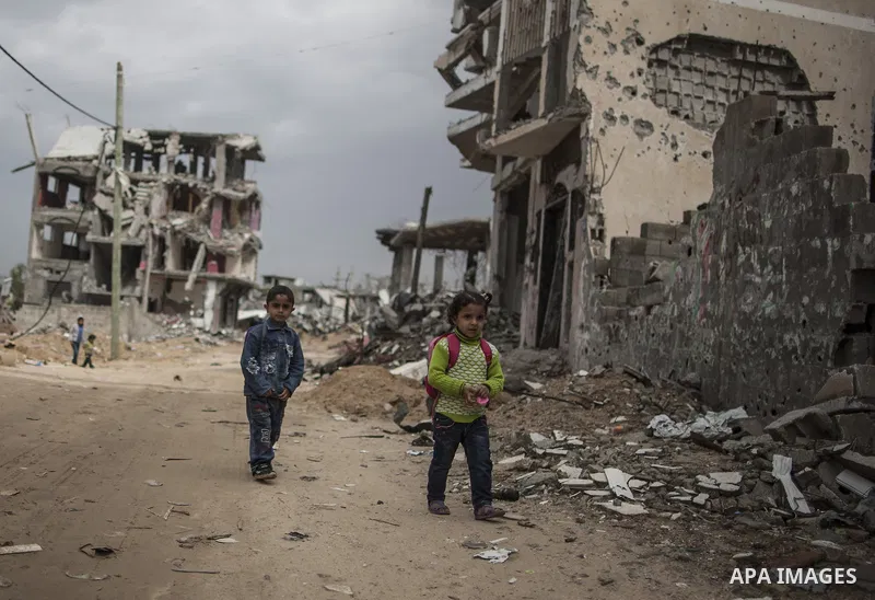 Palestinian children walk along a street of destroyed buildings that witnesses said were destroyed during a seven-week Israeli offensive, on a rainy day in the east of Gaza City October 19, 2014. An open-ended ceasefire...