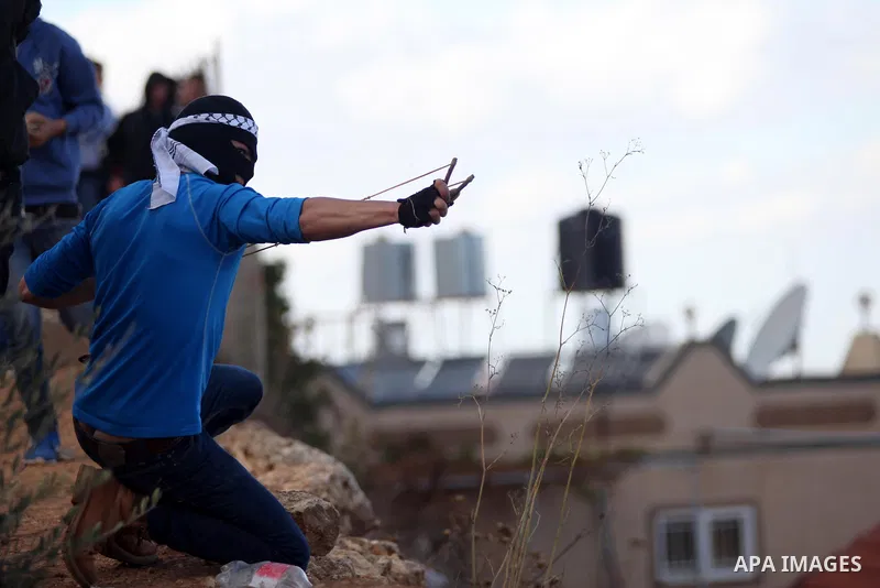 A Palestinian protester uses a sling shot to hurls a stone towards Israeli security forces during clashes following the funeral of kindergarten girl Inas Shawkat Khalil, 5, in the West Bank village of Sinjel north of Ram...