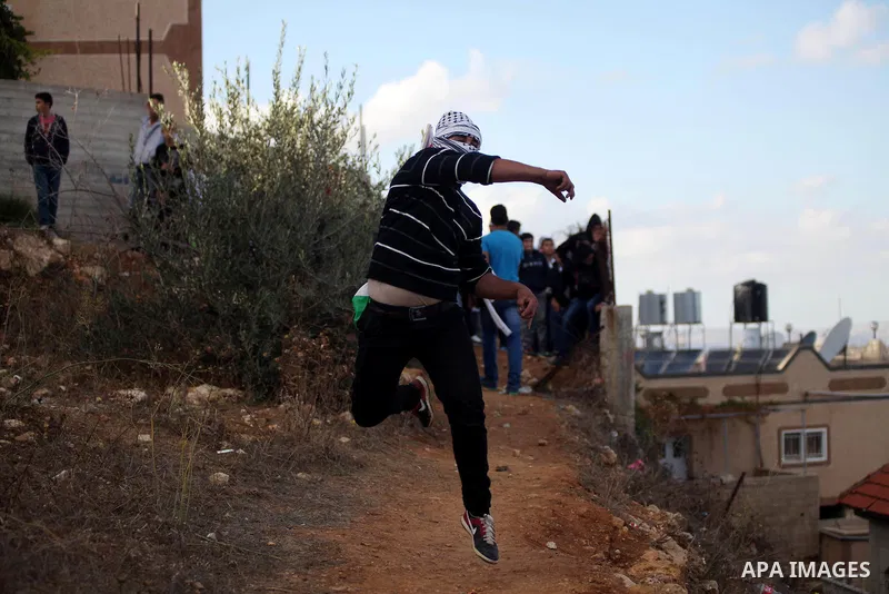 A Palestinian protester throws stones towards Israeli security forces during clashes following the funeral of kindergarten girl Inas Shawkat Khalil, 5, in the West Bank village of Sinjel north of Ramallah, October 20, 20...