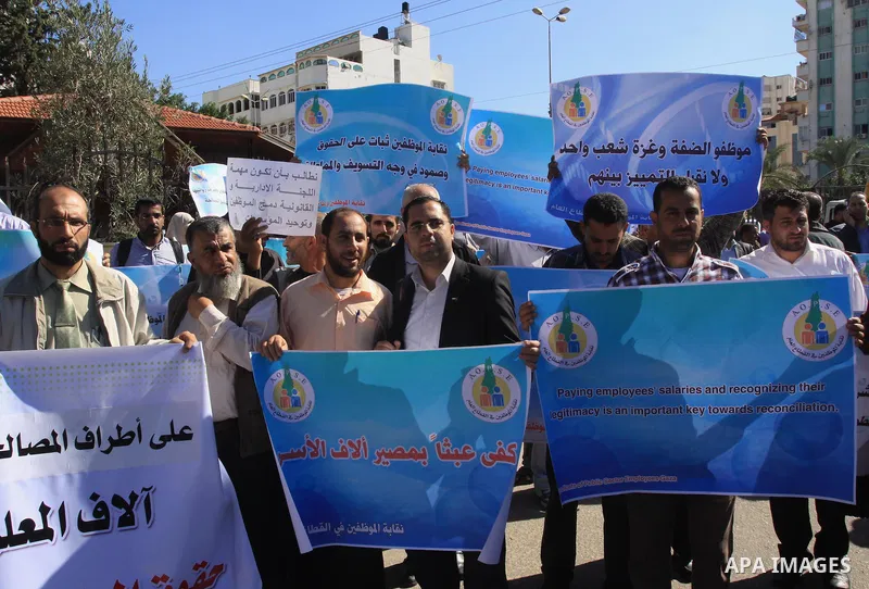 Palestinian employees of the former government in Gaza Strip hold banners during a protest to demanding their salaries, in front of the headquarters of the Council of Ministers in Gaza city, on October 21, 2014. Photo by...