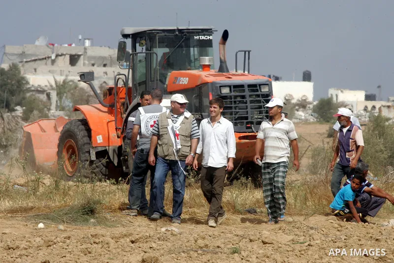 A Palestinian uses a digger in front of International Committee of the Red Cross (ICRC) workers as the comittee assists Palestinian farmers to repair their fields that were devastated during the Israeli army summer's mil...