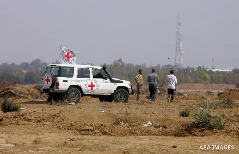 Palestinians stand near an International Committee of the Red Cross (ICRC) vehicle as the comittee assists Palestinian farmers to repair their fields that were devastated during the Israeli army summer's military offensi...