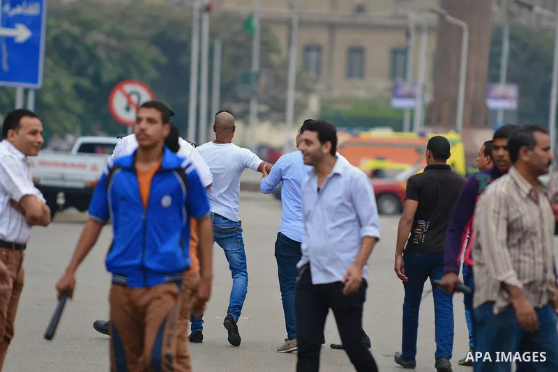 Egyptian students look from a distance to the site of a bomb explosion outside the main gate of Cairo University on October 22, 2014, wounding at least nine people including a senior officer. The assistant police chief o...