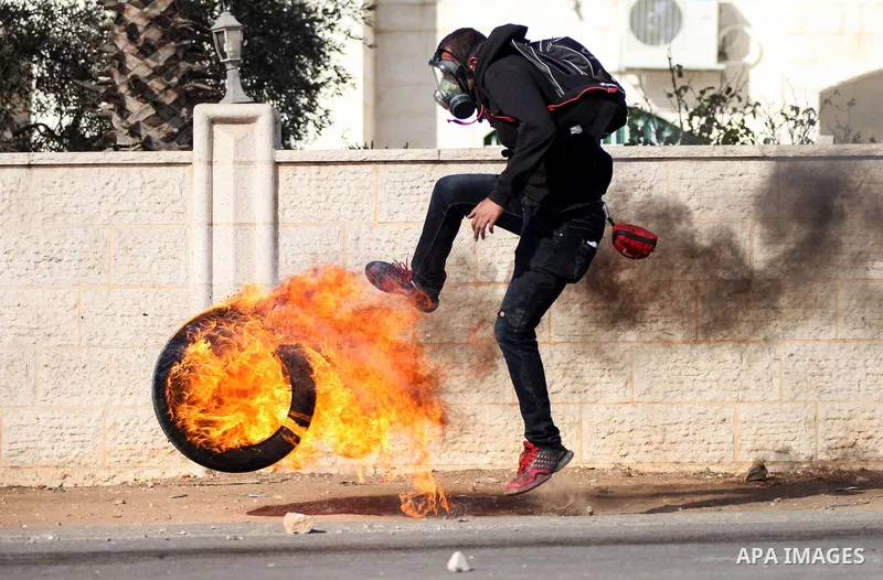 A Palestinian youth kicks a burned tire towards Israeli security forces during clashes after funeral Palestinian-American, Orwah Hammad, 14, who was shot dead last Friday during clashes with Israeli army soldiers, at the...
