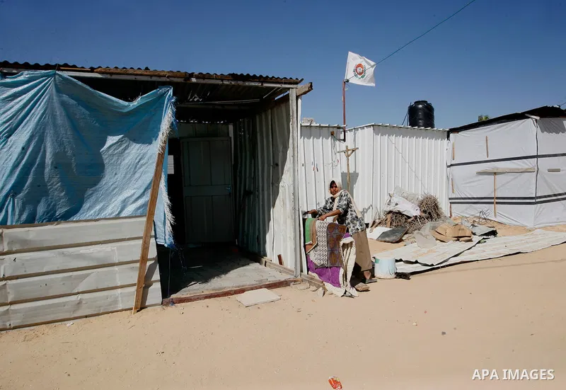 A Palestinian woman stands outside her containers donated by a charity organisation as temporary housing for those whose houses were destroyed during a seven-week Israeli offensive, in Khuzaa, east of Khan Younis, in the...