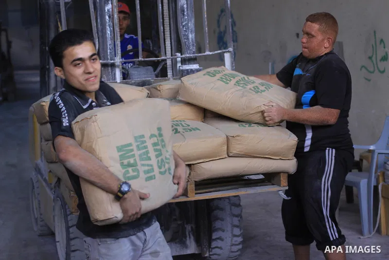 Palestinian workers carry bags of cement as Palestinians, whose houses were partially damaged by what witnesses said was Israeli shelling during the most recent conflict between Israel and Hamas, wait to receive cement o...
