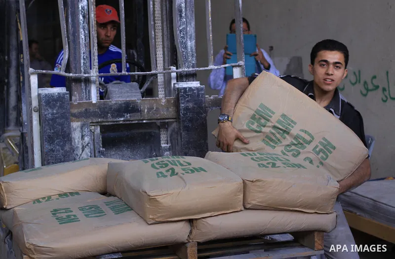 Palestinian workers carry bags of cement as Palestinians, whose houses were partially damaged by what witnesses said was Israeli shelling during the most recent conflict between Israel and Hamas, wait to receive cement o...