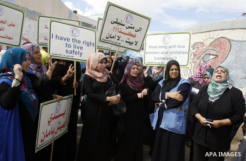 Palestinian women hold placards during a protest in solidarity with women who displaced from their homes during the seven weeks Israeli offensive on Gaza Strip, outside a UN school, in Rafah in the southern Gaza Strip, O...