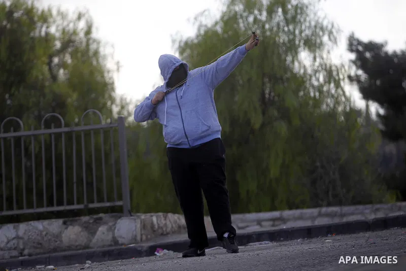 A masked Palestinian youth throw stones at Israeli security forces during clashes after Moataz Higazi was shot in east Jerusalem October 30, 2014. Israeli police shot and killed Higazi suspected of trying to kill a hard-...