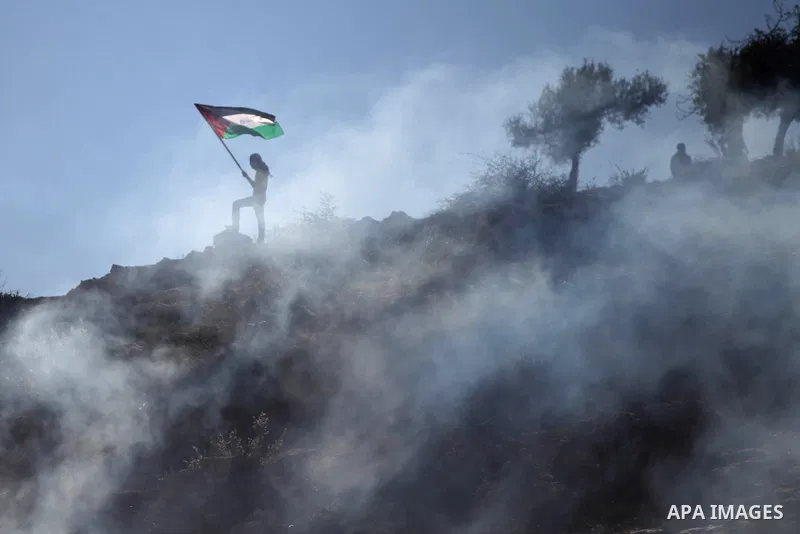 A Palestinian student of the BirZeit University waves his national flag in a cloud of tear gas fired by Israeli security forces during clashes following an anti-Israel demonstration over the recent entry restrictions to...
