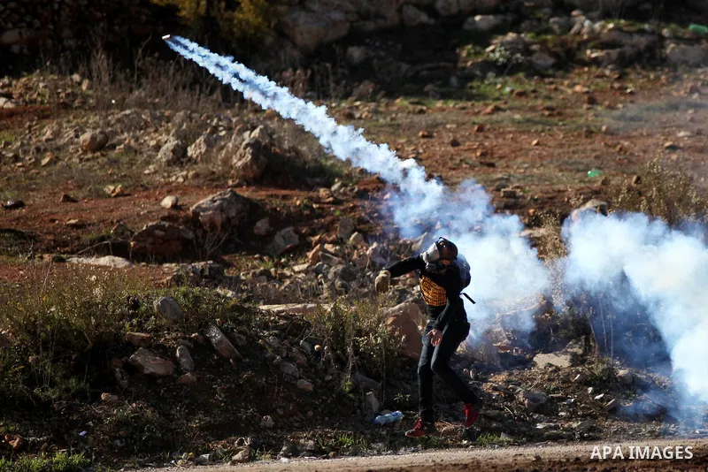A Palestinian student of the Birzeit University throws back a tear gas canister fired by Israeli security forces during clashes following an anti-Israel demonstration over the recent entry restrictions to the al-Aqsa mos...