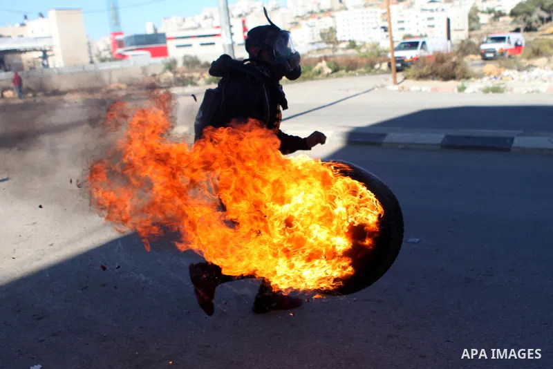 A Palestinian student of the BirZeit University holds a burning tire during clashes with Israeli security forces following an anti-Israel demonstration over the recent entry restrictions to the al-Aqsa mosque, outside Is...