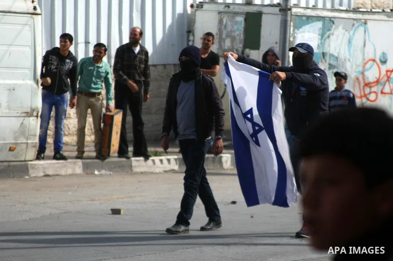 A Palestinian protester holds an Israeli flag during clashes with Israeli security forces following a protest against Israel's restrictions at the Al-Aqsa Mosque in Jerusalem, in the West Bank city of Hebron, November 14...