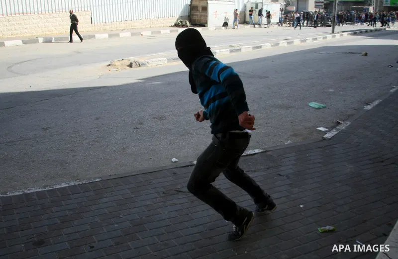 A Palestinian protester throws stones towards Israeli security forces during clashes following a protest against Israel's restrictions at the Al-Aqsa Mosque in Jerusalem, in the West Bank city of Hebron, November 14, 201...