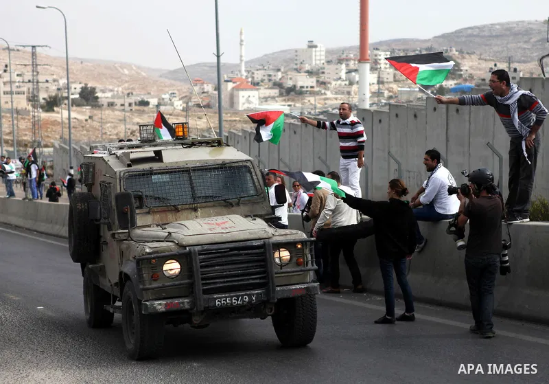 Palestinian protesters hold their national flags in front of an Israeli security forces vehicle during a demonstration against Israel's restrictions at the Al-Aqsa Mosque in Jerusalem, in Hizma village near the West Bank...