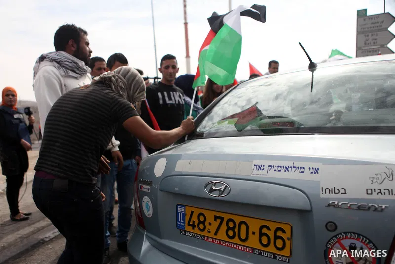 A Palestinian protester hangs his national flag on an Israeli car during a demonstration against Israel's restrictions at the Al-Aqsa Mosque in Jerusalem, in Hizma village near the West Bank city of Ramallah, November 14...
