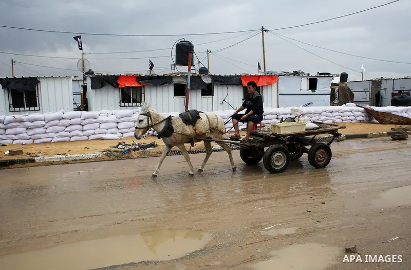A Palestinian man ride a donkey cart on a rainy day past the temporary homes of Palestinian that witnesses said was destroyed by Israeli shelling during the most recent conflict between Israel and Hamas in Khan Younis in...
