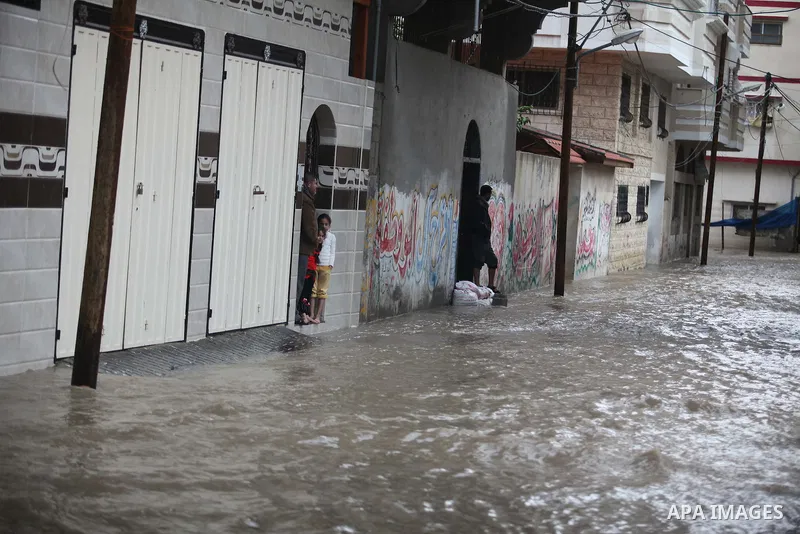 Palestinians stand in front of their family house during heavy rain in Gaza City, on November 27, 2014 as a fierce winter storm which has been battering the region for the past four days. Photo by Ashraf Amra