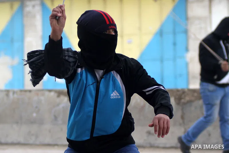 A Palestinian protester uses a slingshot to throw a stone towards Israeli security forces during clashes following a protest against Israeli restrictions to Al-Aqsa Mosque in Jerusalem, at the Qalandia checkpoint near th...