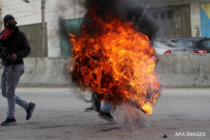 A Palestinian protester holds a burning tire during clashes with Israeli security forces following a protest against Israeli restrictions to Al-Aqsa Mosque in Jerusalem, at the Qalandia checkpoint near the West Bank city...