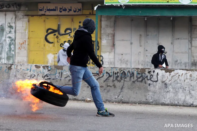 A Palestinian protester holds a burning tire during clashes with Israeli security forces following a protest against Israeli restrictions to Al-Aqsa Mosque in Jerusalem, at the Qalandia checkpoint near the West Bank city...