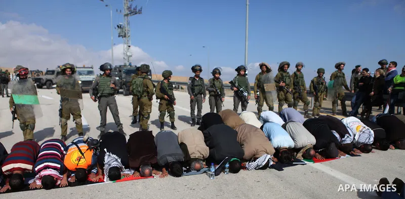 Palestinian protesters pray as Israeli soldiers and border policemen stand guard as they try to block a highway between Jerusalem and the Dead Sea near the West Bank town of Jericho Friday, Nov. 28, 2014. Photo by Shadi...