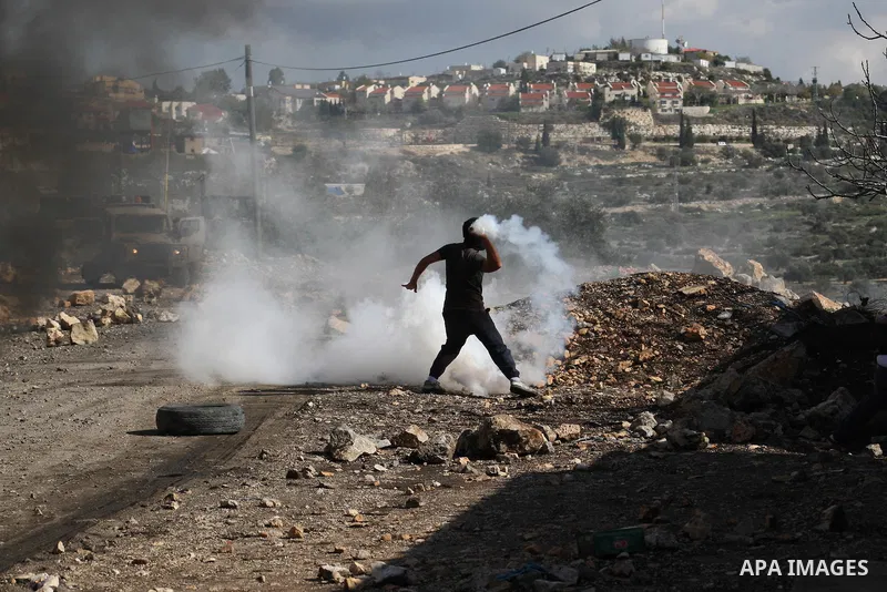 A Palestinian protester throws back a tear gas canister fired by at Israeli security forces during clashes in a protest against the expropriation of Palestinian land by Israel following Friday prayers in the village of K...