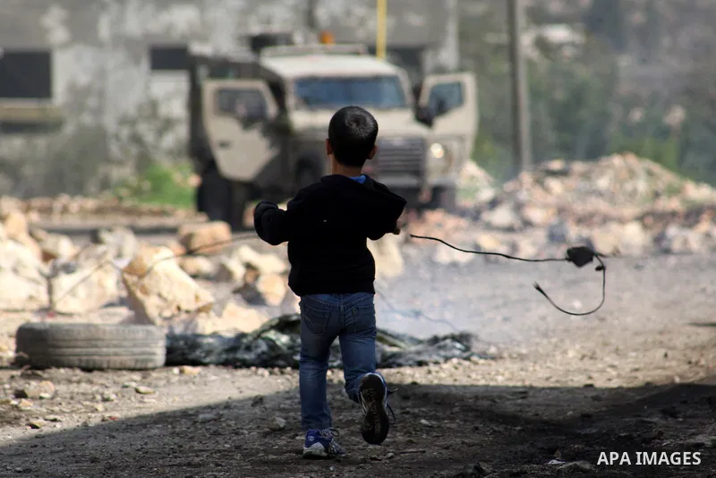 A Palestinian boy uses a slingshot to throw stones at Israeli security forces during clashes in a protest against the expropriation of Palestinian land by Israel following Friday prayers in the village of Kafr Qaddum, ne...