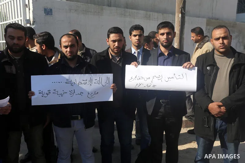 Palestinian employees hold banners during a protest demanding their salaries, in front of the headquarters of the Ministry of Labour, in Gaza city on November 30, 2014. Photo by Mohammed Asad