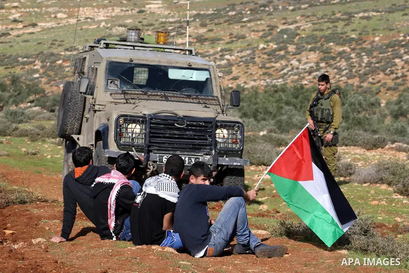 Palestinian children waving a Palestinian flag, set in front of Israeli soldiers as they stand guard at an agricultural land in Salem village, near the West Bank city of Nablus, December 5, 2014. Many groves are effectiv...