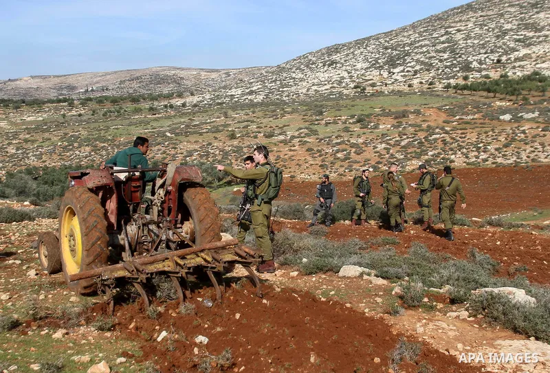 An Israeli soldier speaks with a Palestinian farmer as he works at his field in Salem village, near the West Bank city of Nablus, December 5, 2014. Many groves are effectively off limits to Palestinians or threatened wit...