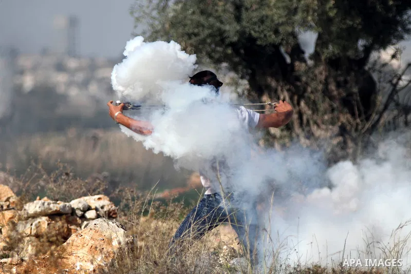 A Palestinian protester uses a slingshot to throw back a tear gas canister fired by Israeli security forces during clashes following a demonstration against Israel's controversial barrier, in the outskirts of the village...