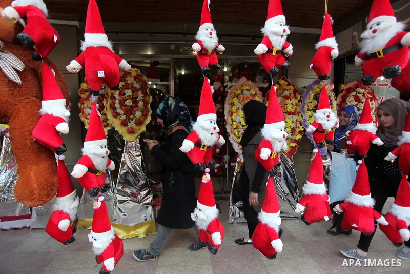 Palestinians walk past a shop decorated with santa claus toys, celebrating the Christmas holiday in Gaza city on December 24, 2014. Photo by Ashraf Amra