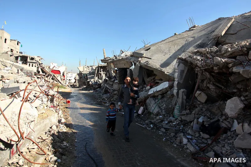 A Palestinian man carrying his son walks in front the rubble of houses which were destroyed during the recent Israeli offensive on Gaza Strip, in Shijaiyah neighborhood, east Gaza city December 25, 2014. Photo by Ashraf...
