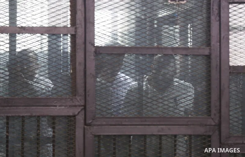 Defendants stand in a courtroom cage during the retrial of Alaa Abdel Fattah and 24 others, in Cairo on December 27, 2014. The defendants were sentenced in June to 15 years in prison for holding an unlicensed and violent...