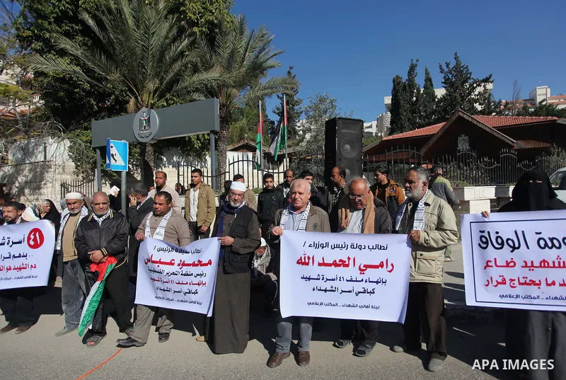 Palestinian families of martyrs hold placards during a protest to demand their rights, in front of the headquarters of the Council of Ministers in Gaza city, on December 31, 2014. Photo by Ashraf Amra