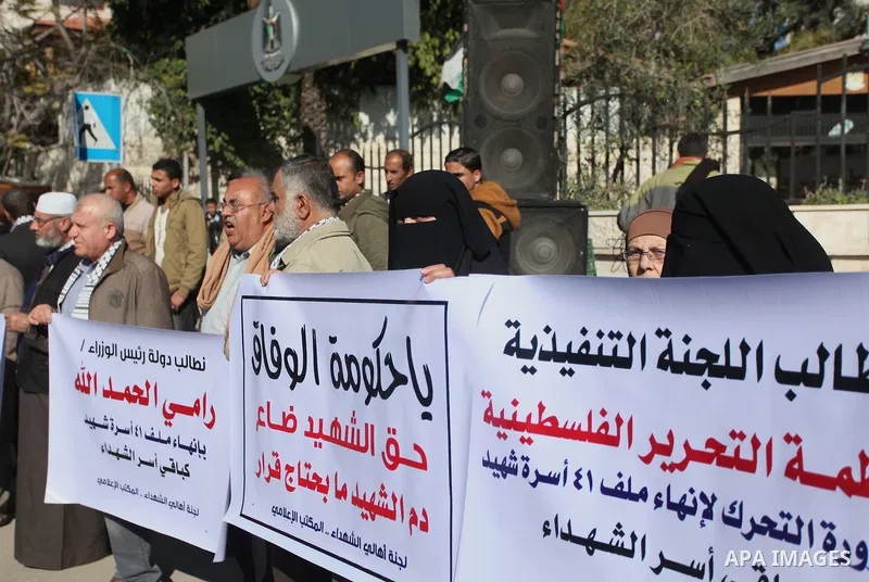 Palestinian families of martyrs hold placards during a protest to demand their rights, in front of the headquarters of the Council of Ministers in Gaza city, on December 31, 2014. Photo by Ashraf Amra